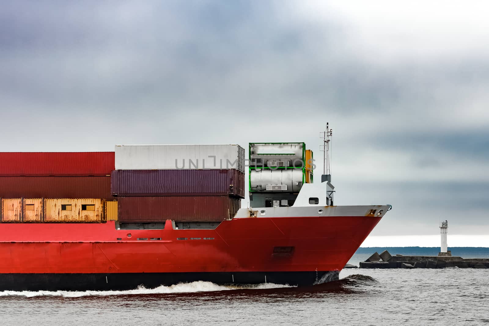 Red cargo container ship's bow in cloudy day