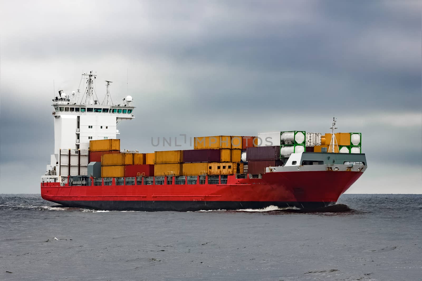 Red cargo container ship sailing from Baltic sea in cloudy day