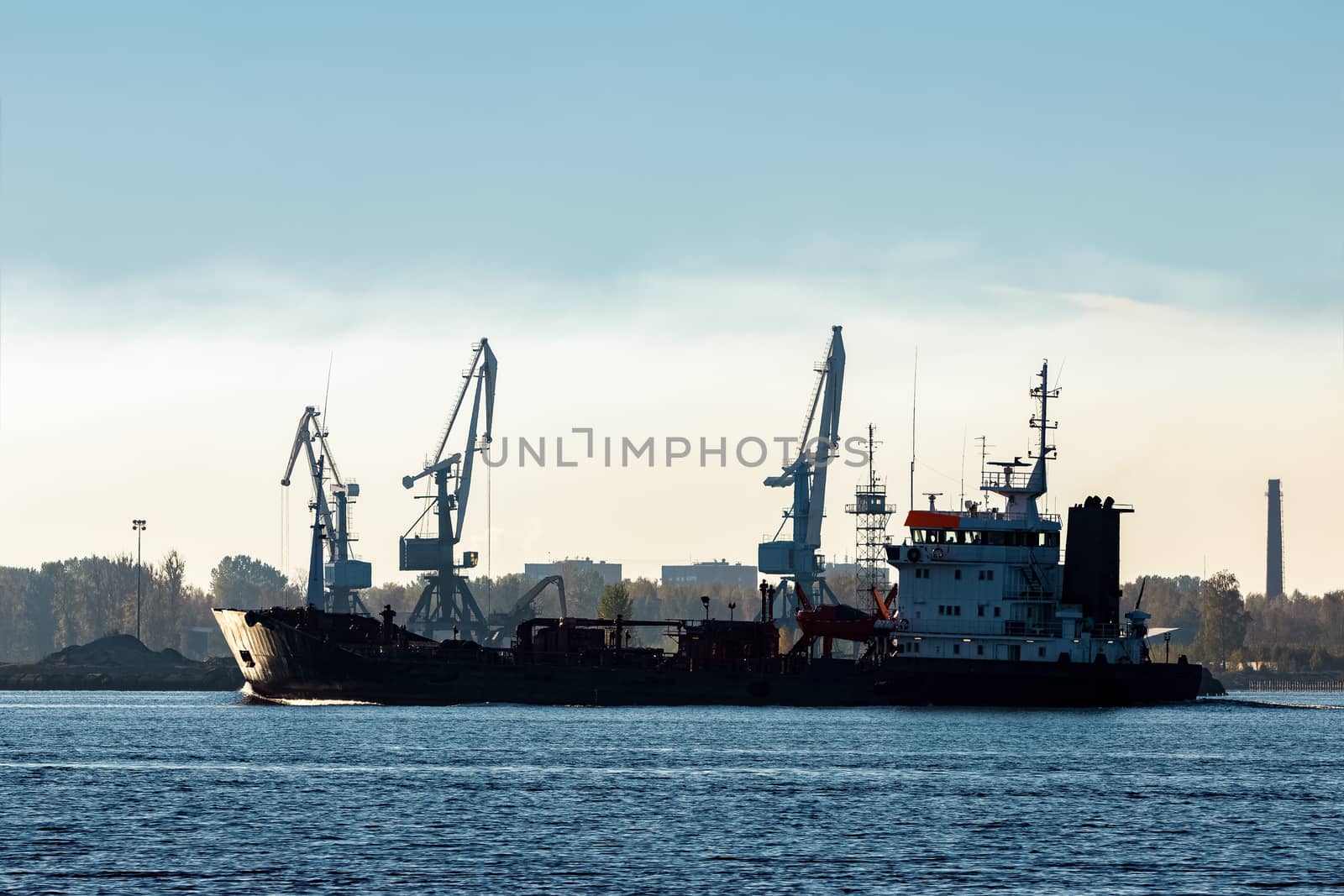 Black cargo oil tanker moving past the cargo cranes