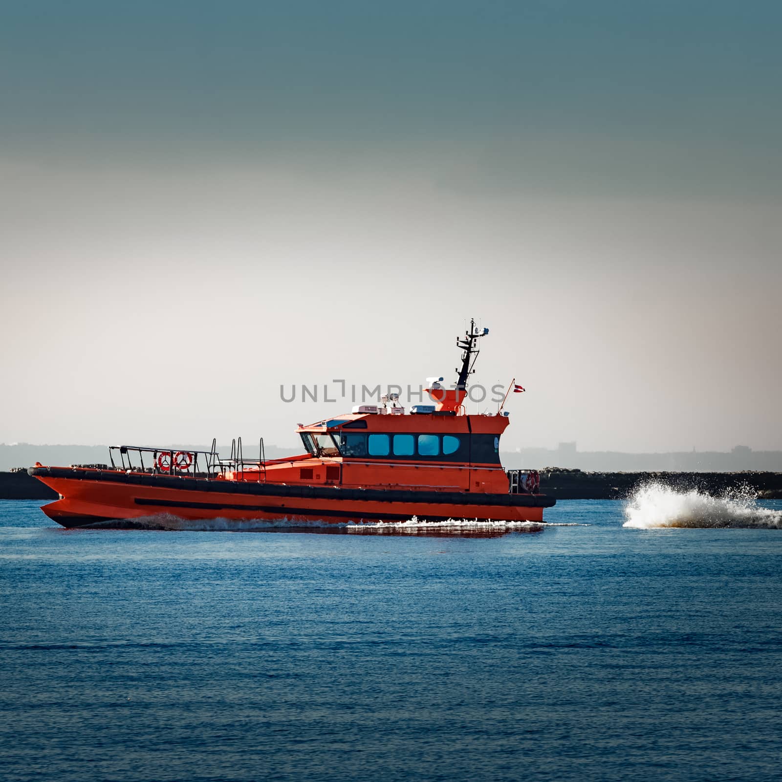 Red pilot ship moving at speed past the breakwater dam