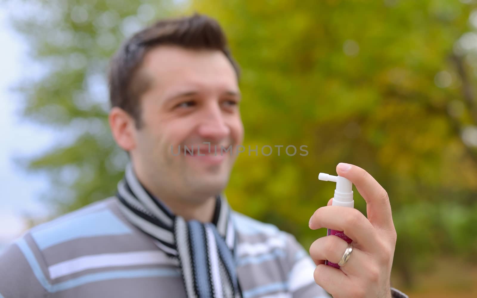 Young man using throat spray in cold season