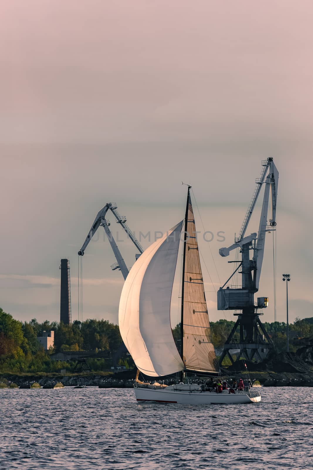 Sailboat moving past the cargo cranes in evening, Latvia