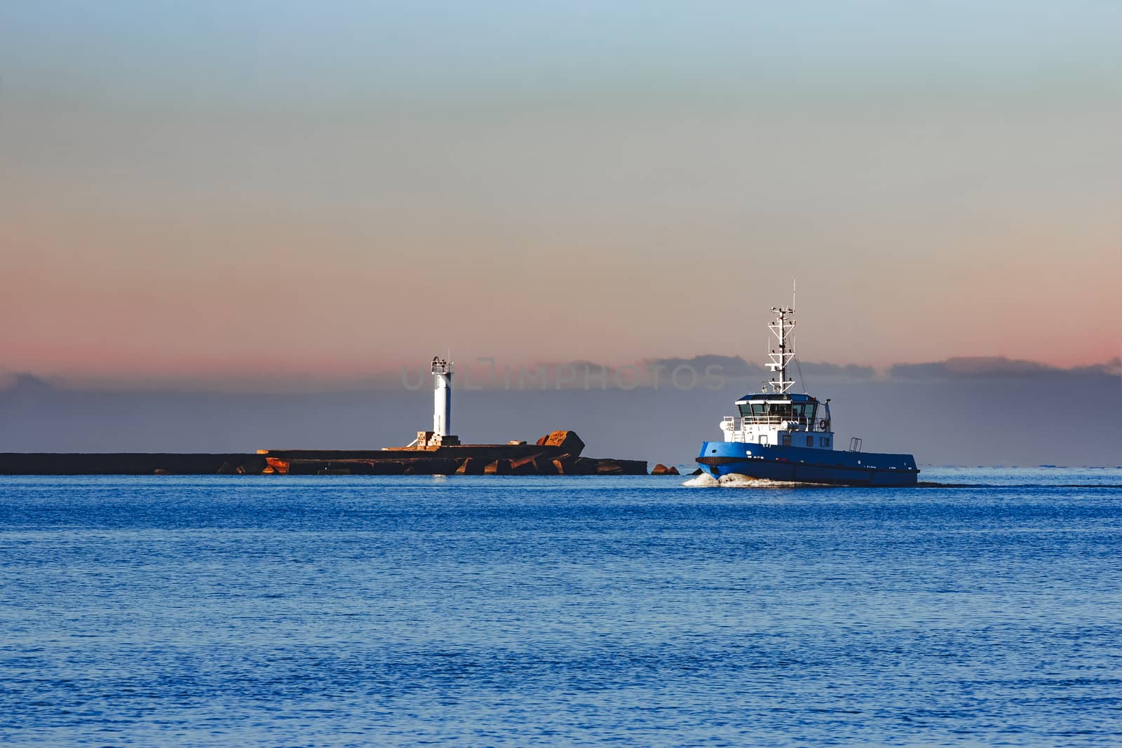 Blue small tug ship sailing past the breakwater dam in morning