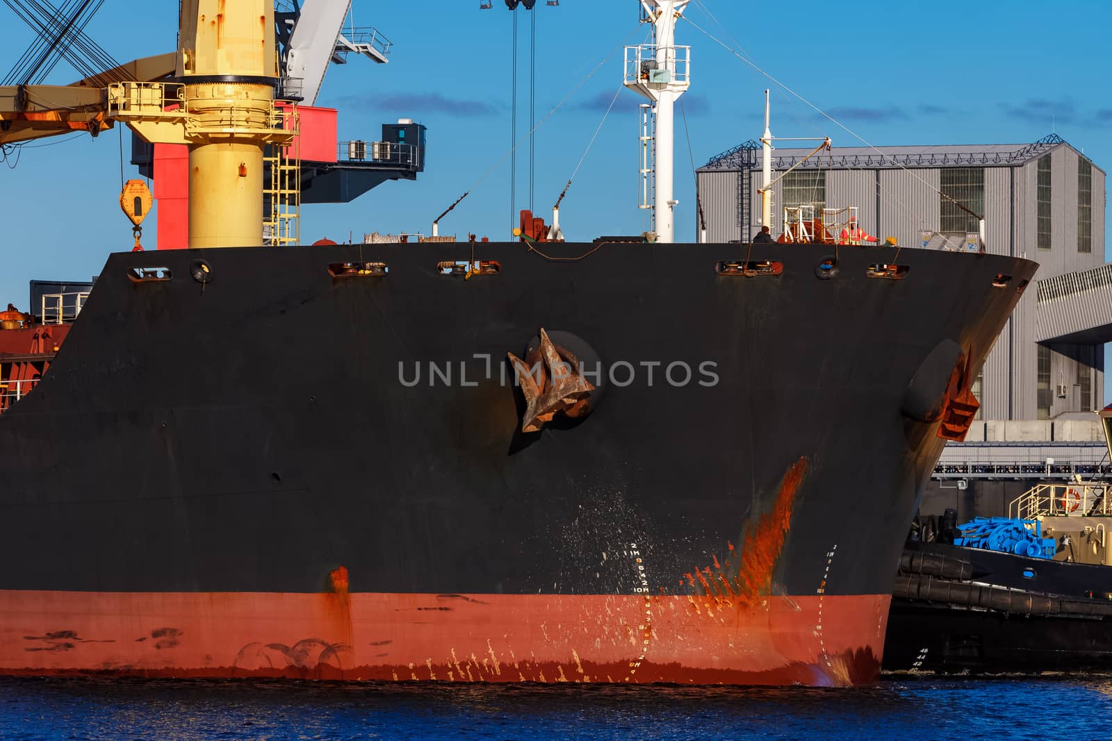 Black cargo ship mooring at the port with tug ship support