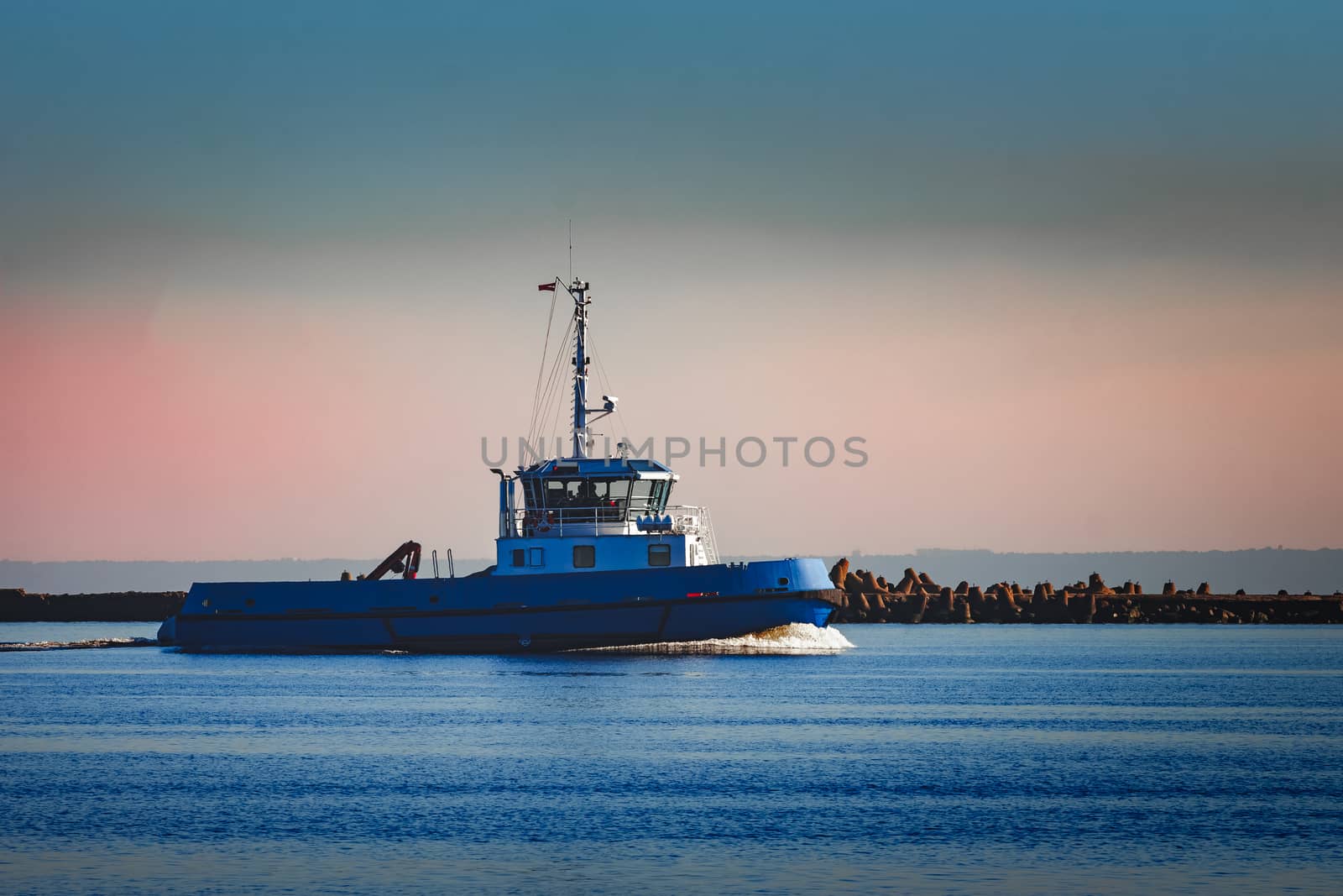 Blue small tug ship sailing past the breakwater dam in morning