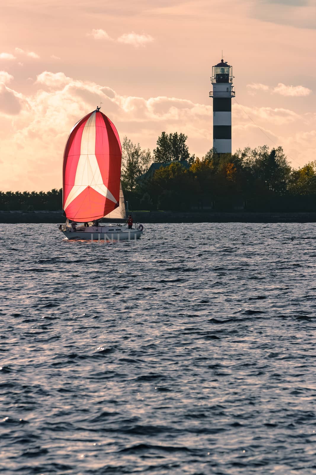 Red sailboat sailing past the big lighthouse by sengnsp