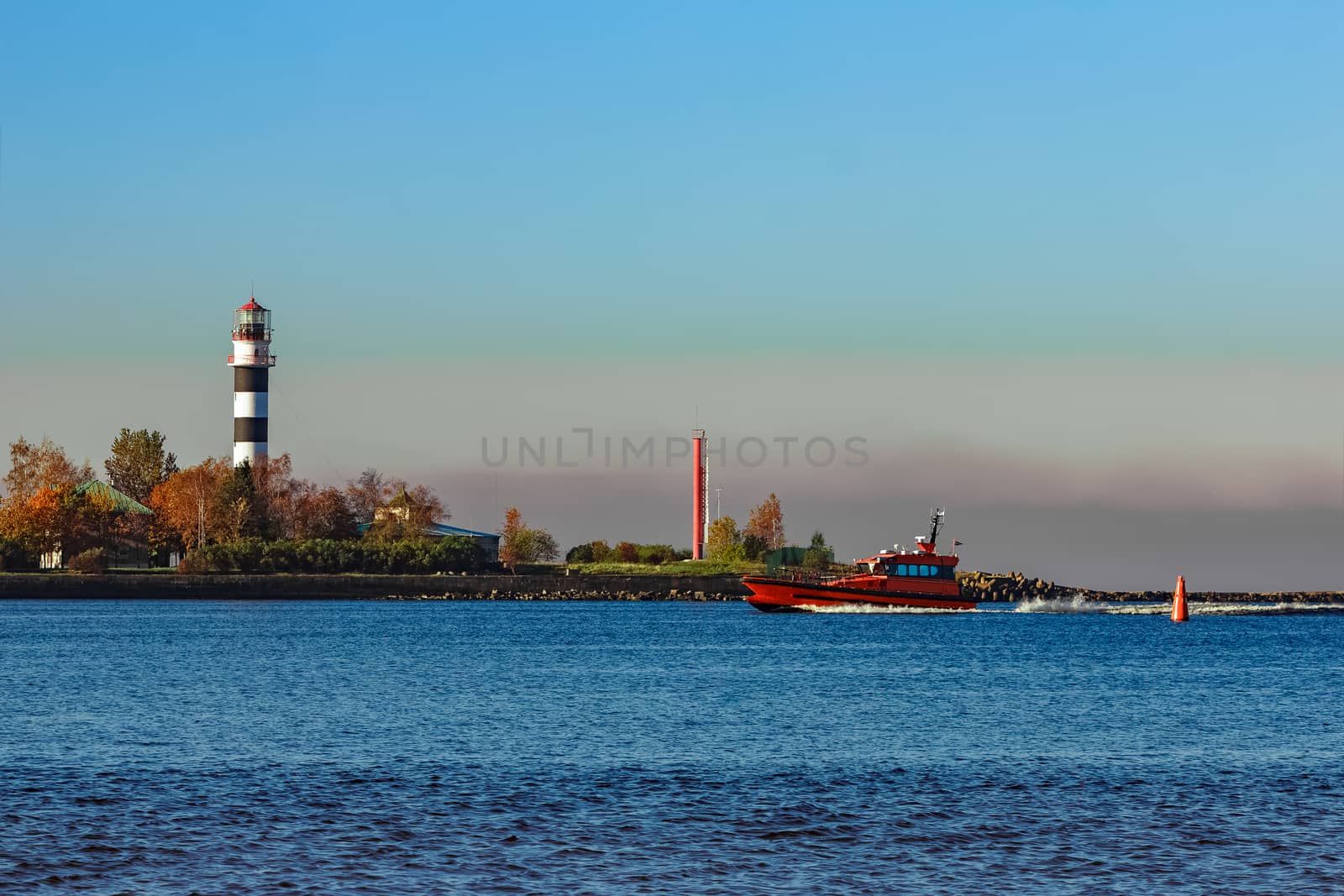 Red pilot ship moving past the lighthouse in Riga