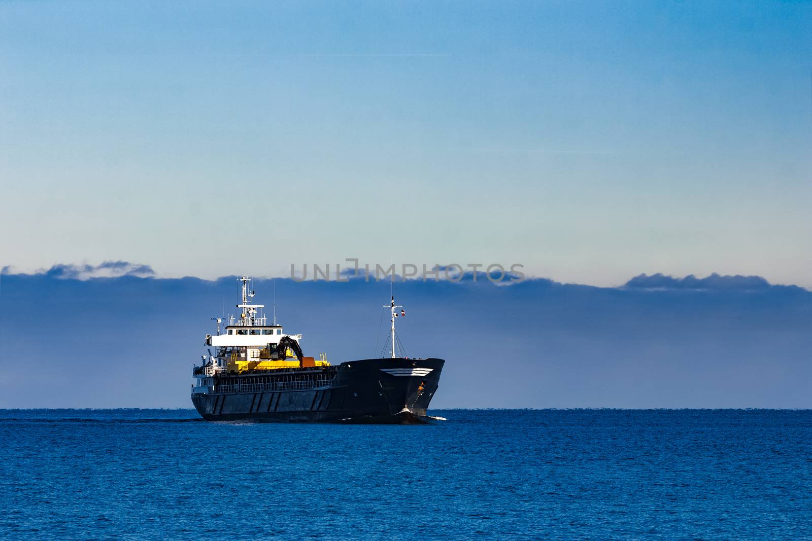 Black cargo ship with long reach excavator moving by baltic sea