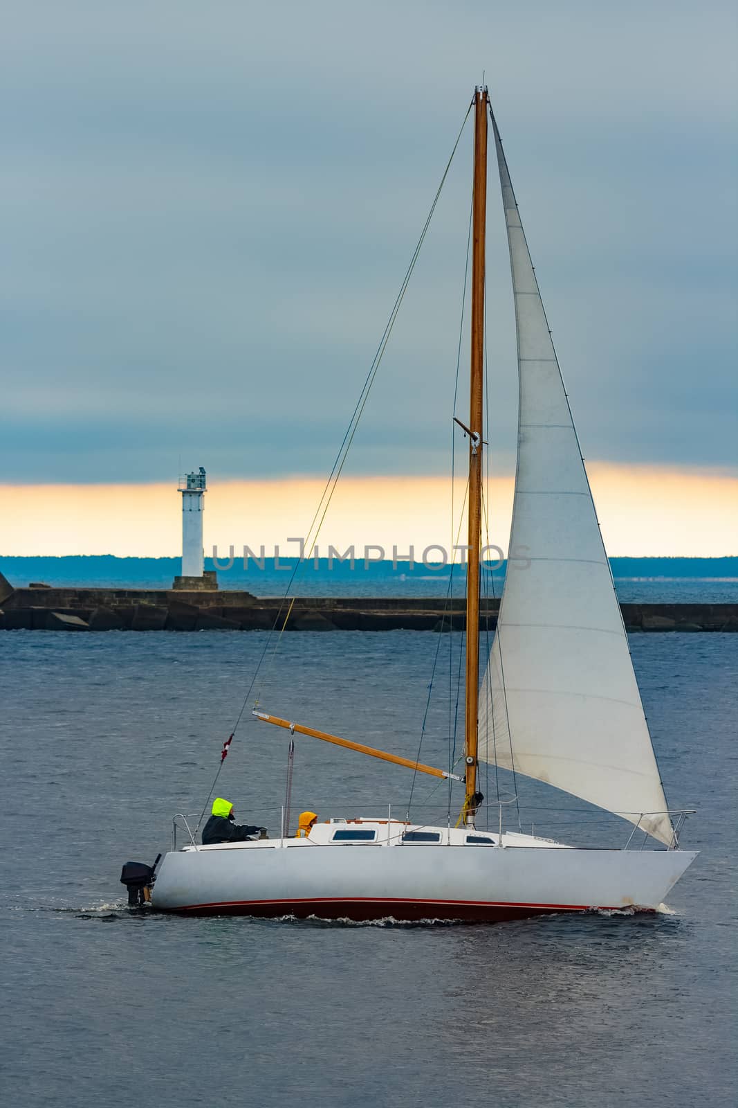 White sailboat traveling past the lighthouse in Riga