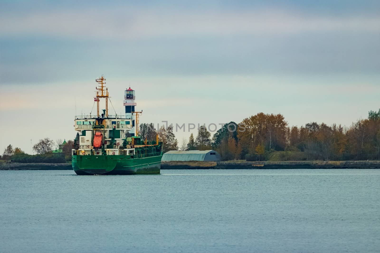 Green cargo ship moving to the port in cloudy day