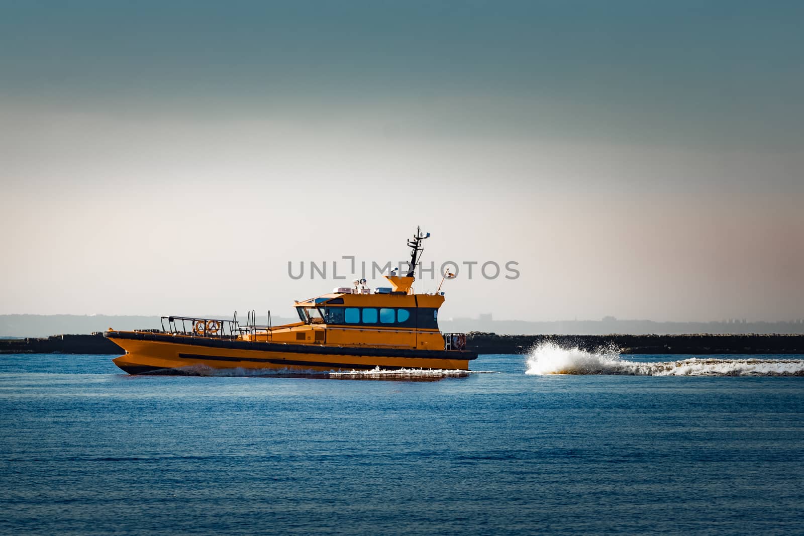 Orange pilot ship moving at speed past the breakwater dam