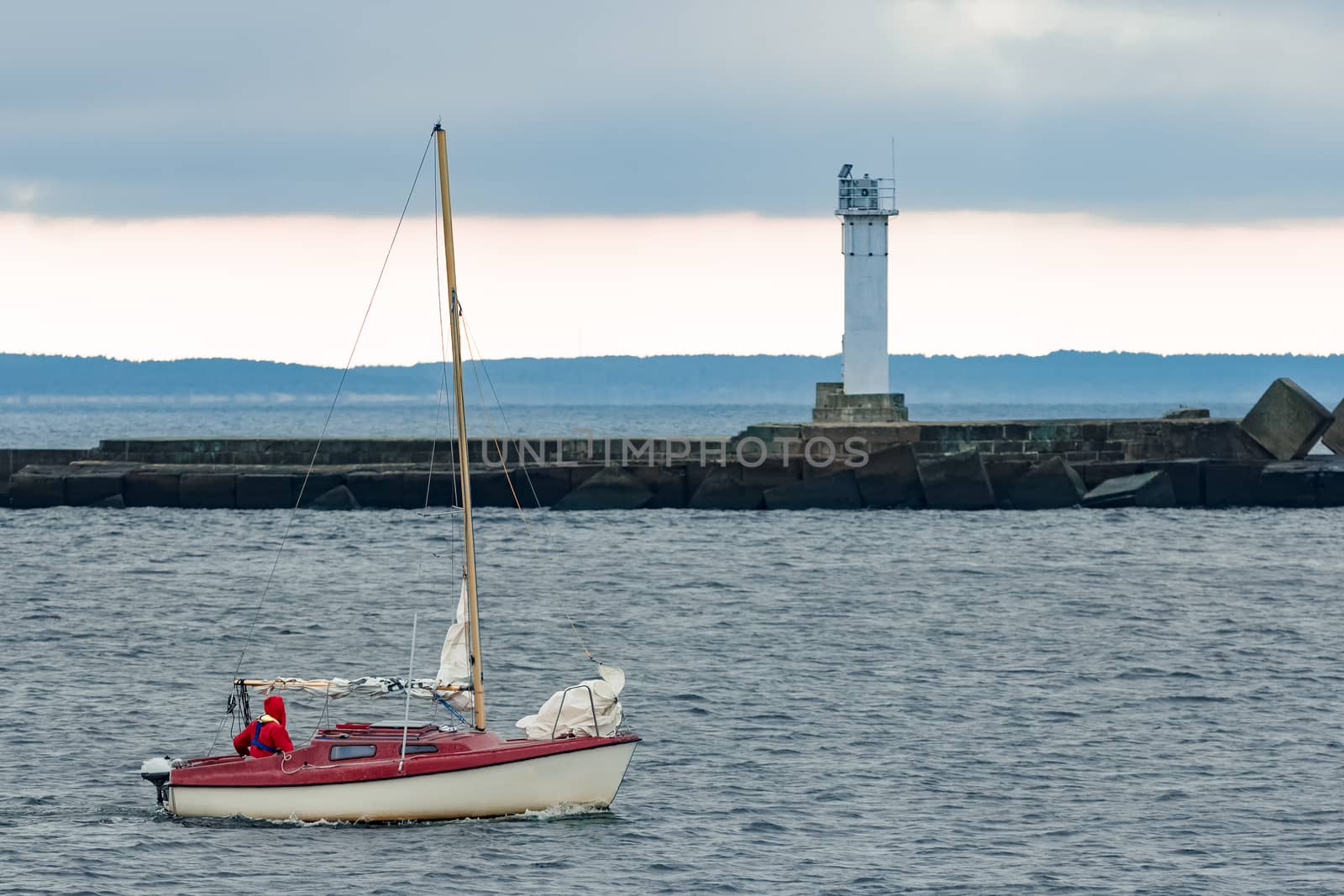 Red sailboat traveling past the lighthouse in Riga