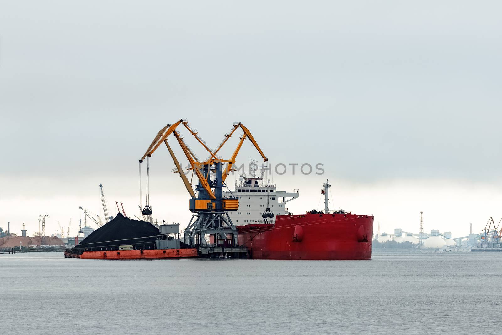 Large red cargo ship loading with a coal in the port