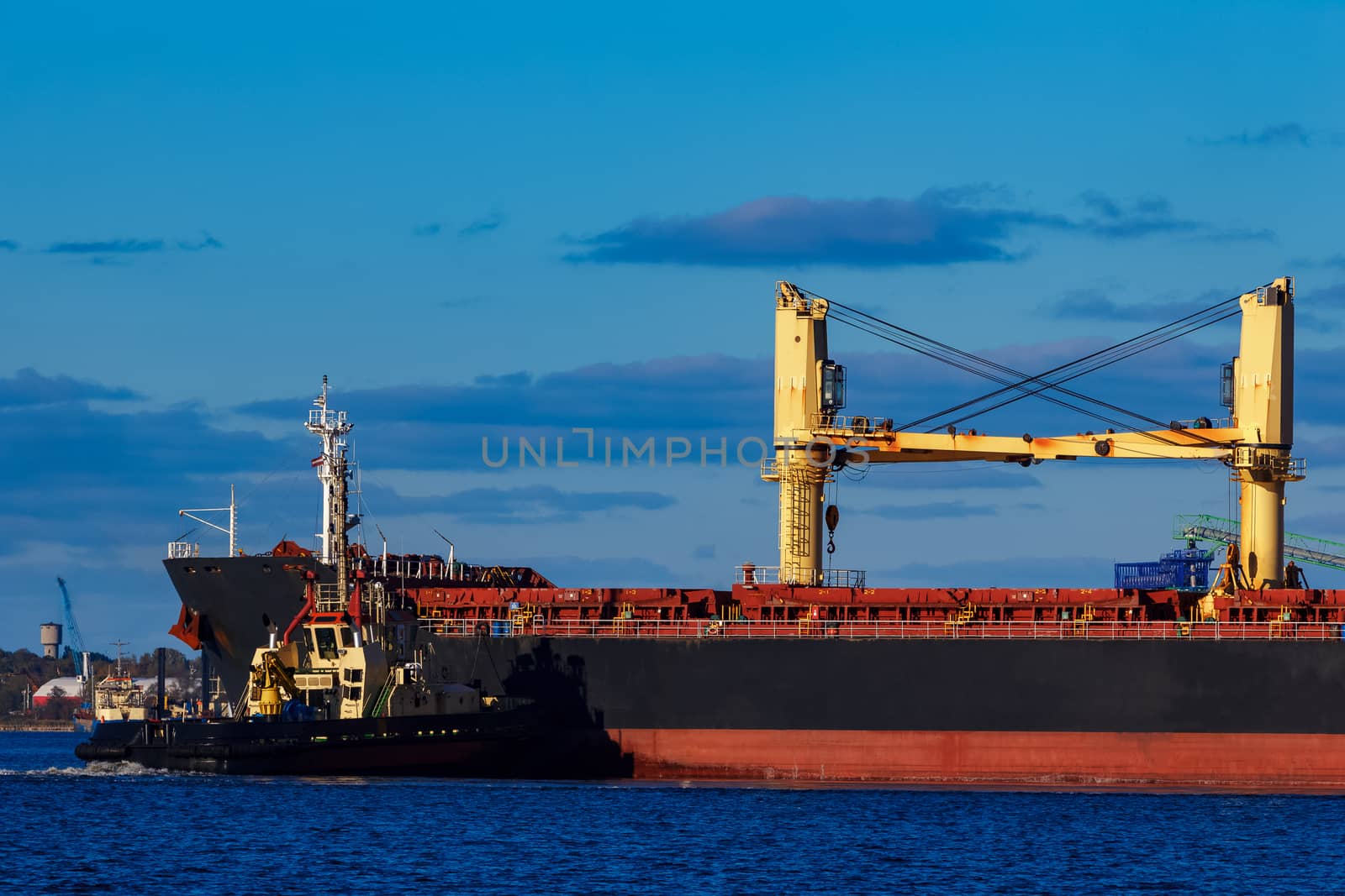 Black cargo ship mooring at the port with tug ship support