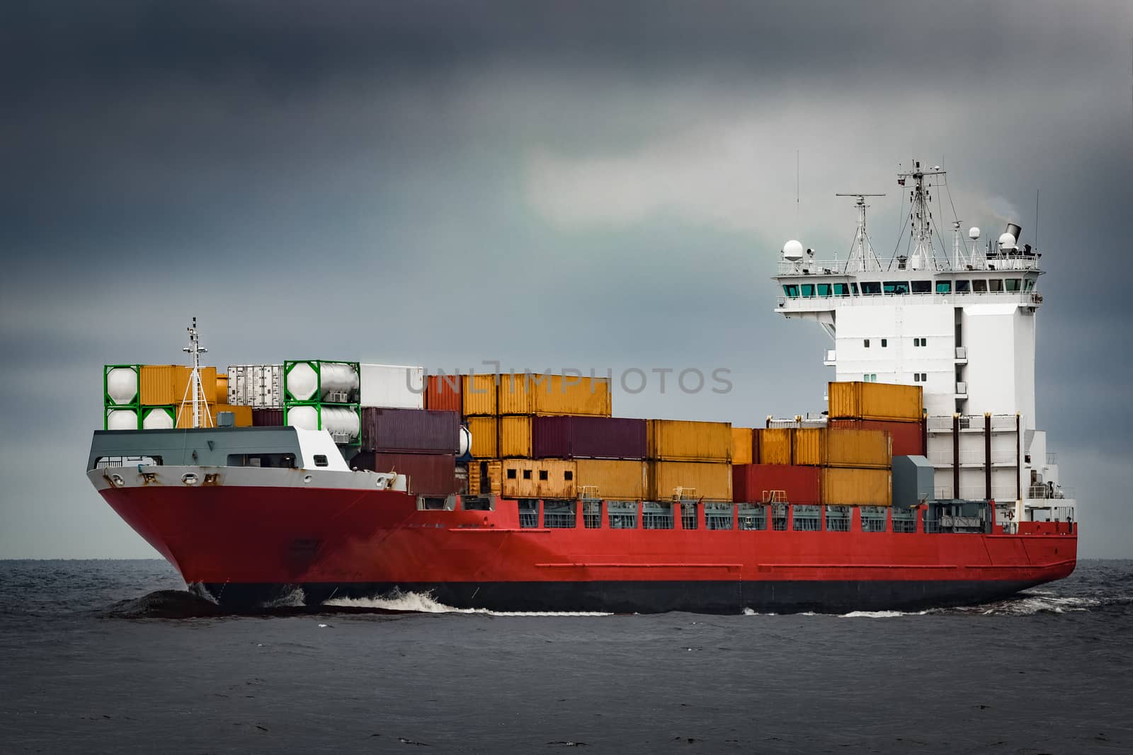 Red cargo container ship sailing from Baltic sea in cloudy day