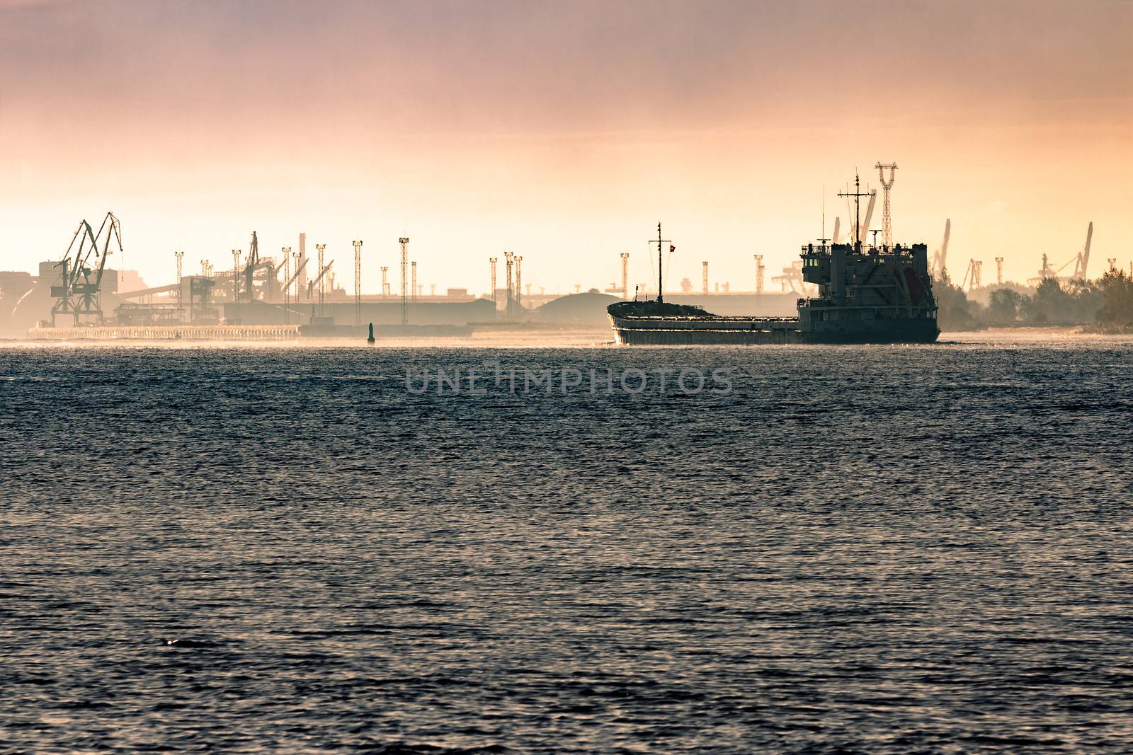 Cargo ship silhouette entering a port of Riga at the morning