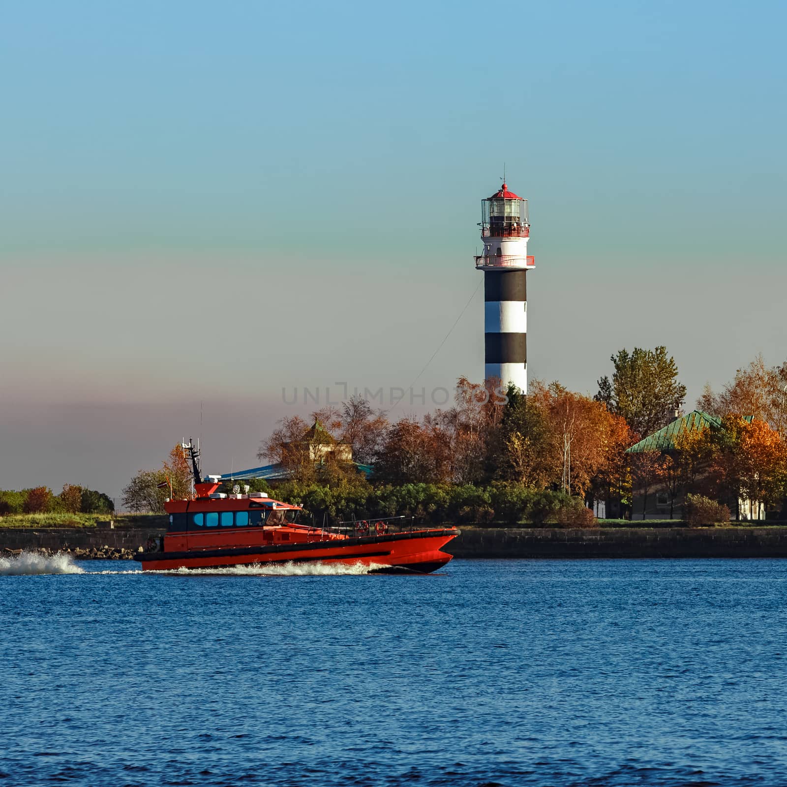 Red pilot ship moving past the lighthouse in Riga