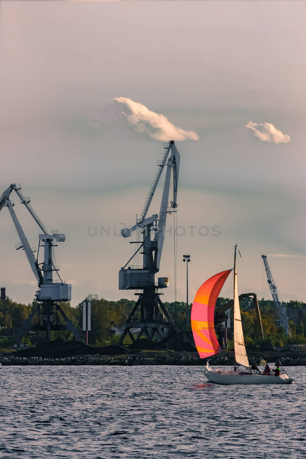 Sailboat moving past the cargo cranes in evening, Latvia