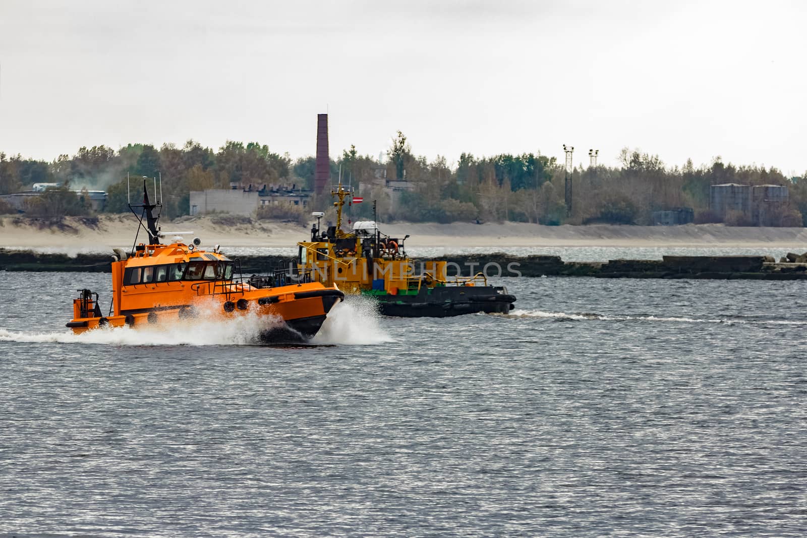 Orange pilot ship moving at speed past the tug ship in Riga