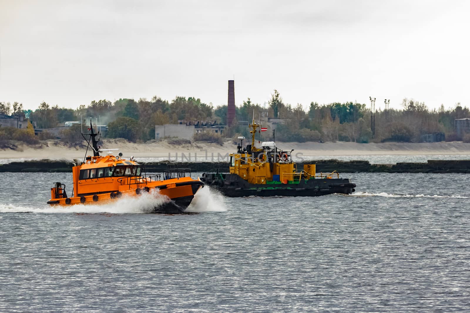 Orange pilot ship moving at speed past the tug ship in Riga