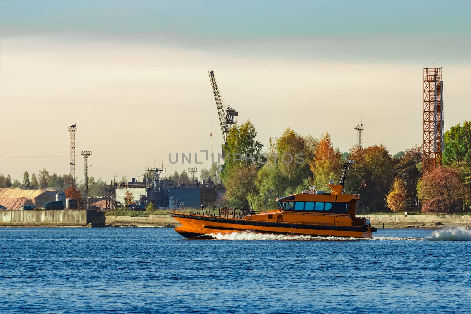 Orange pilot ship sailing past the autumn trees in Europe