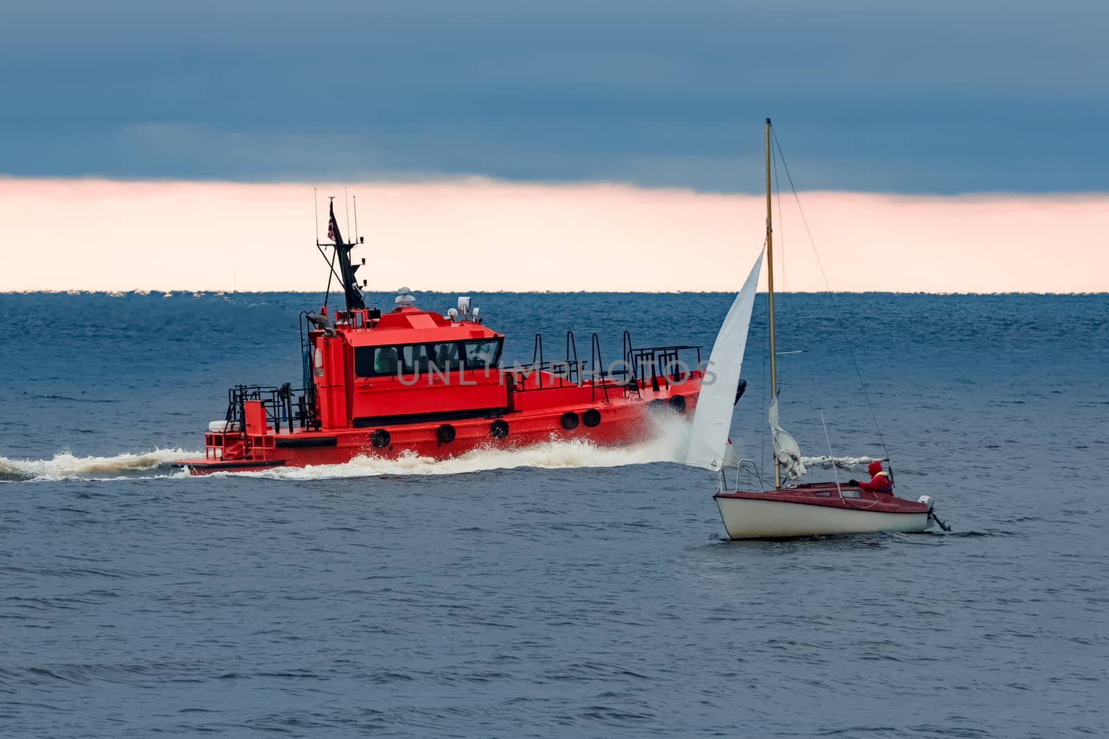 Red pilot ship moving at speed past the sailboat in Baltic sea