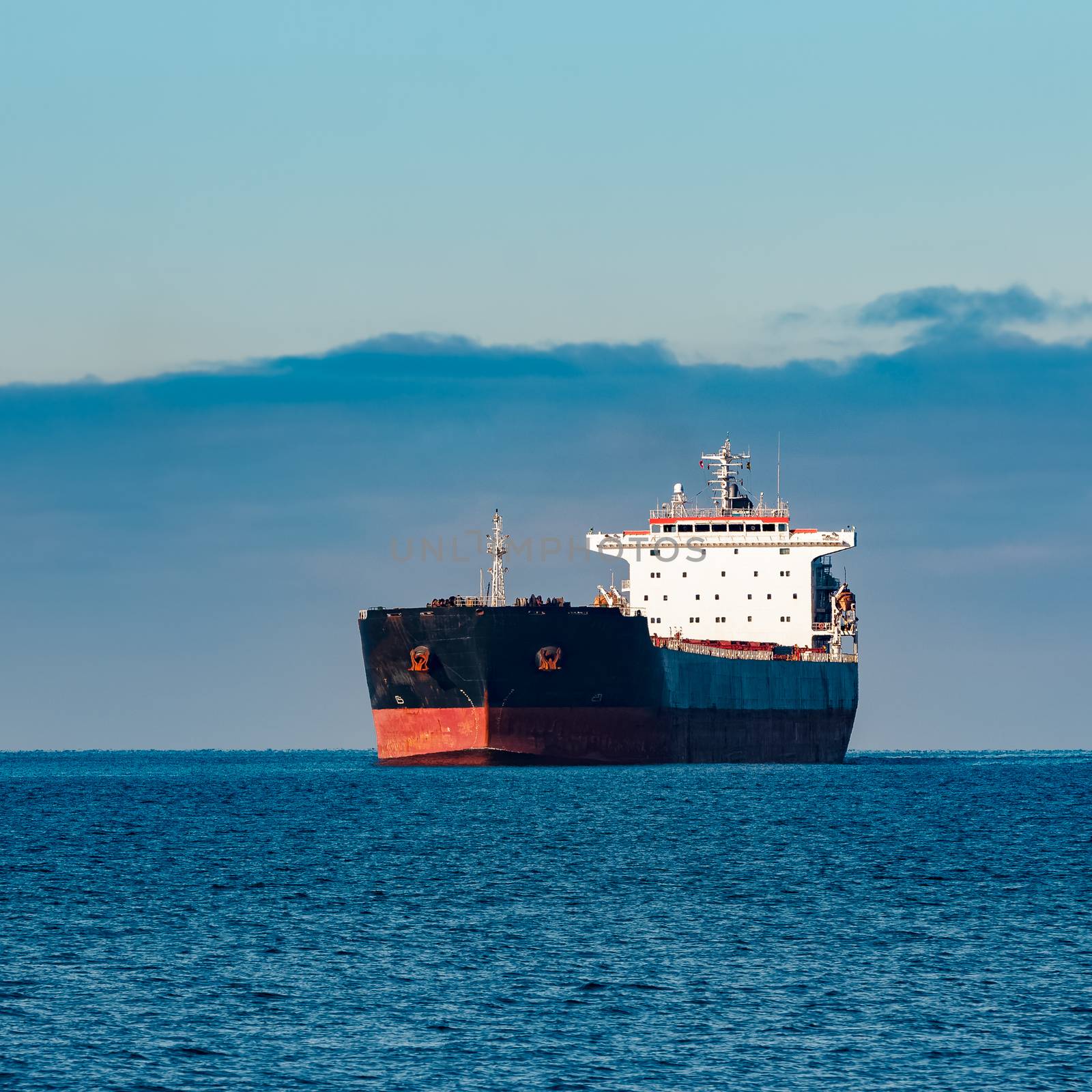 Black cargo ship moving in still Baltic sea water. Riga, Europe