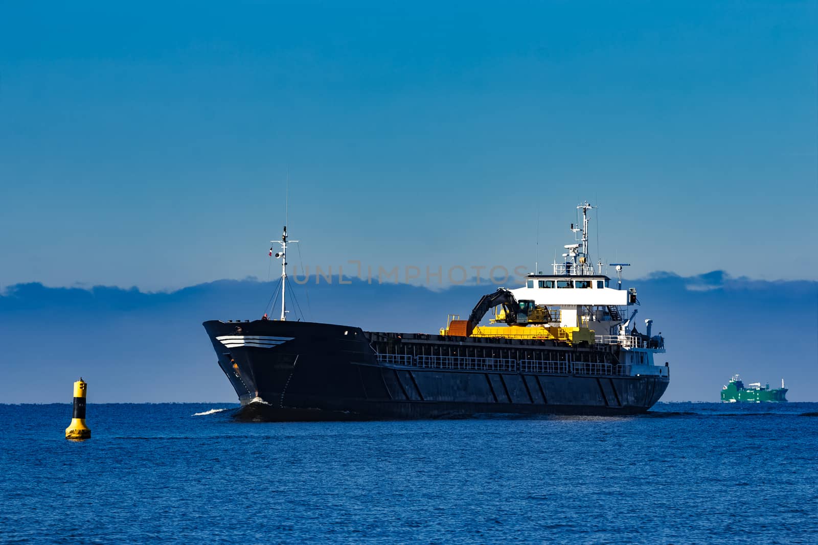 Black cargo ship with long reach excavator moving by baltic sea