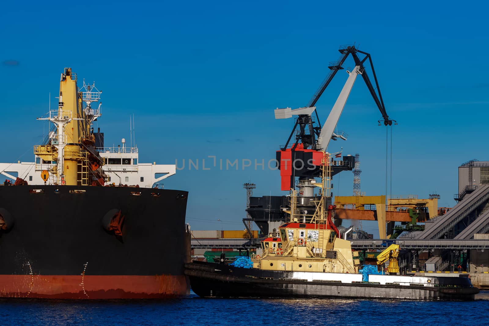 Black cargo ship mooring at the port with tug ship support