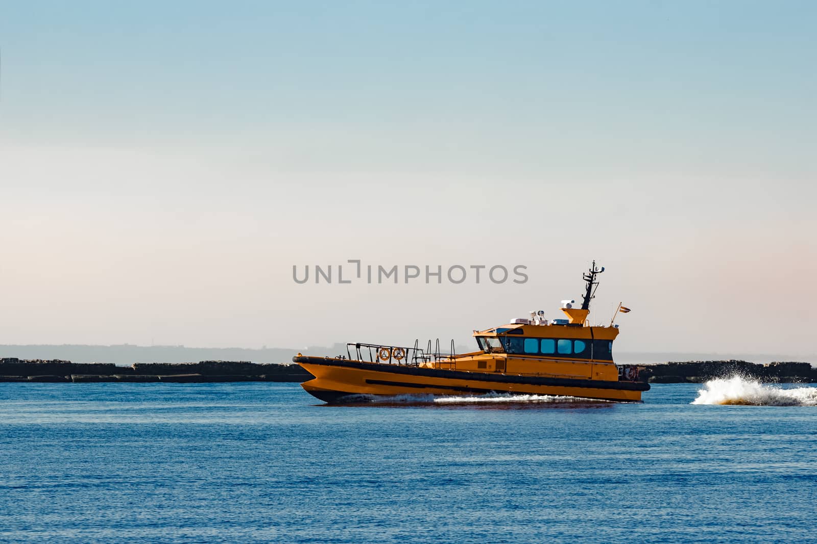 Orange pilot ship moving at speed past the breakwater dam