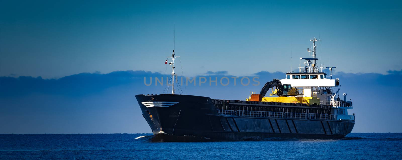 Black cargo ship with long reach excavator moving by baltic sea