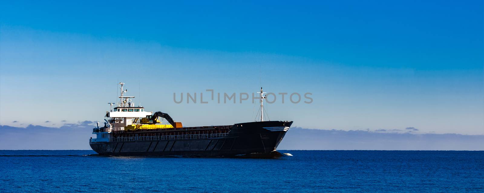 Black cargo ship with long reach excavator moving by baltic sea