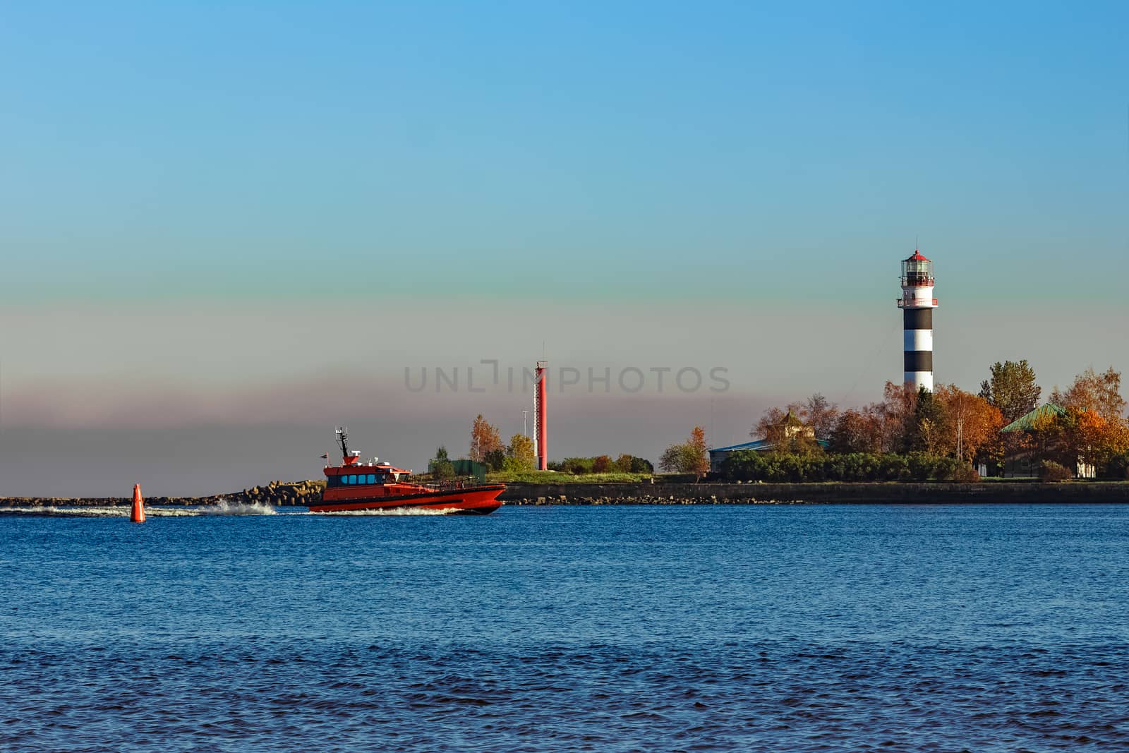 Red pilot ship moving past the lighthouse in Riga