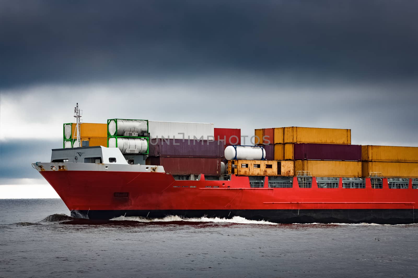 Red cargo container ship's bow in cloudy day