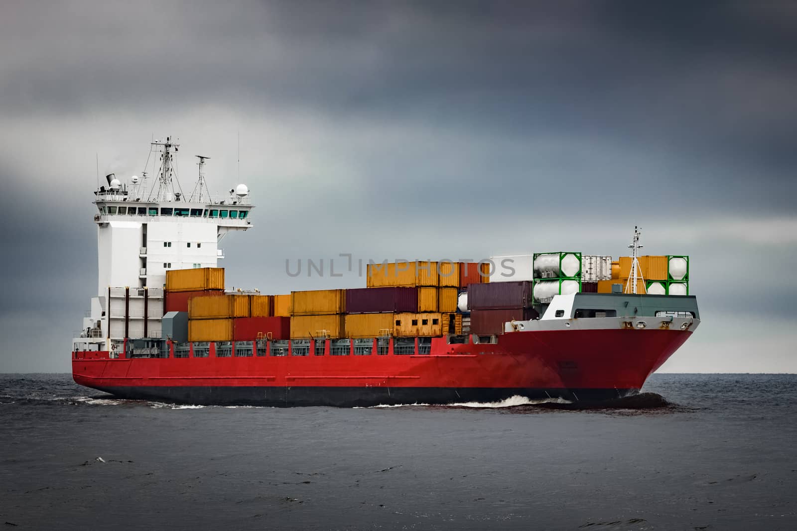 Red cargo container ship sailing from Baltic sea in cloudy day