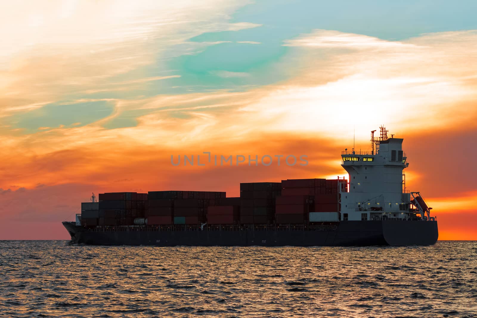 Blue container ship leaving Riga city during hot sunset