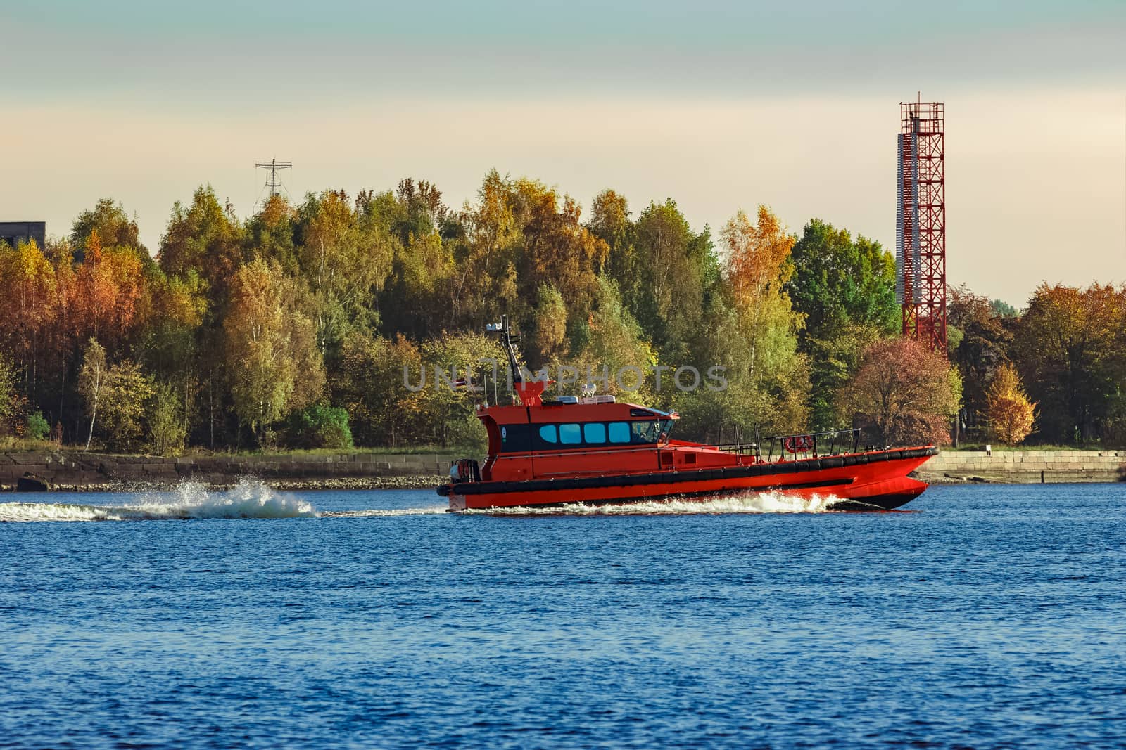 Red pilot ship moving past the autumn trees in Europe