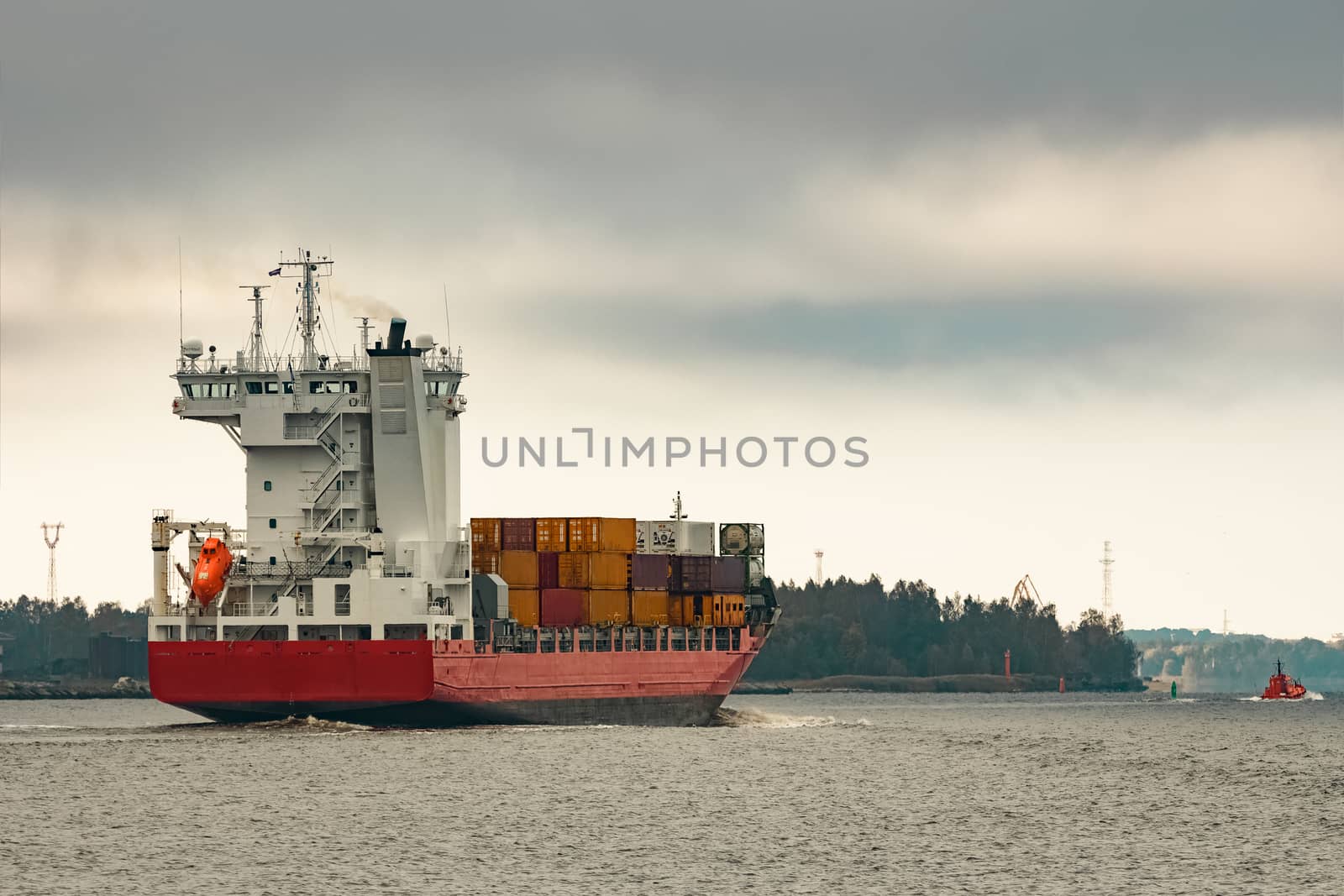 Red cargo container ship entering the port of Riga in cloudy day