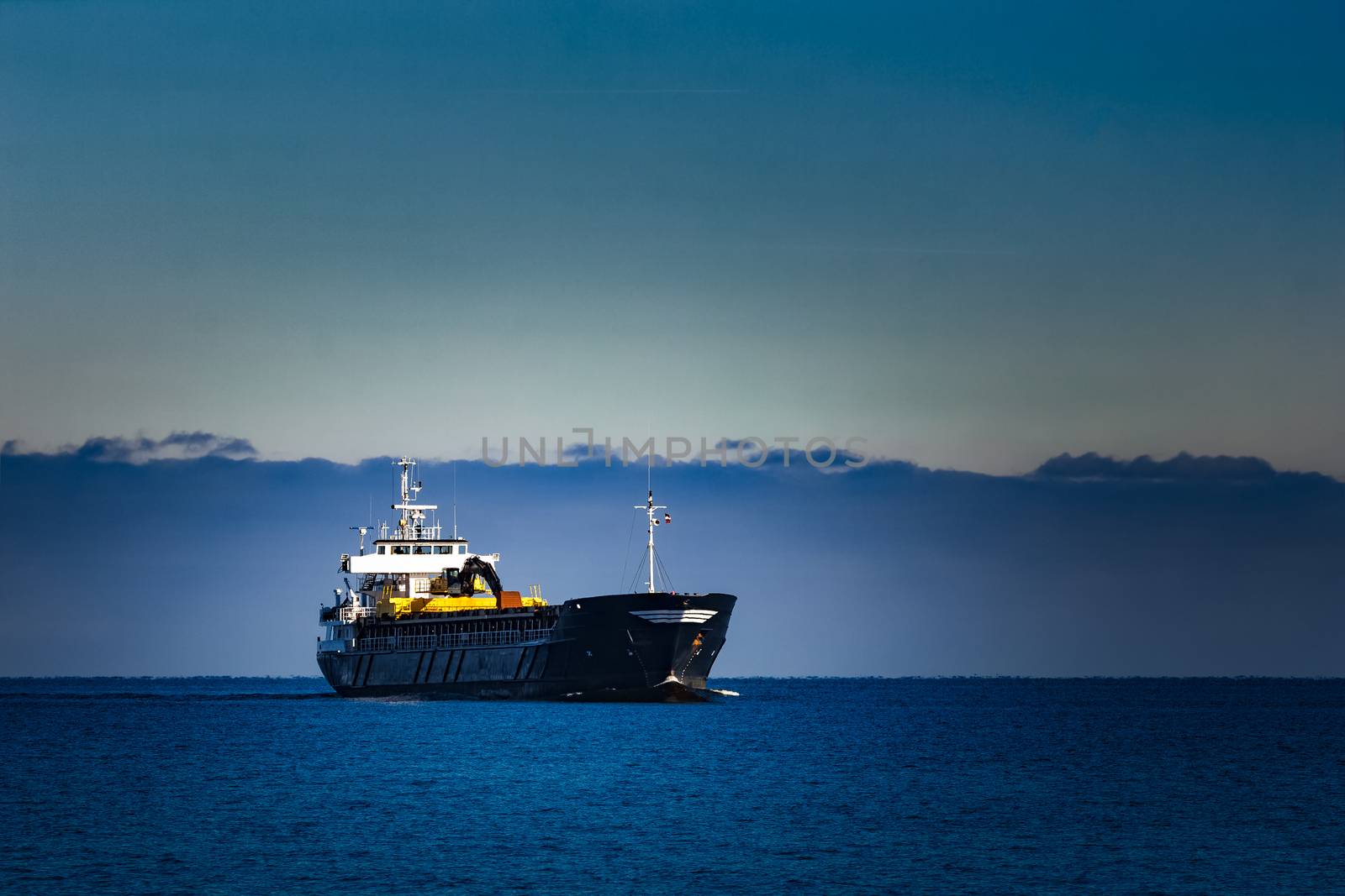 Black cargo ship with long reach excavator moving by baltic sea