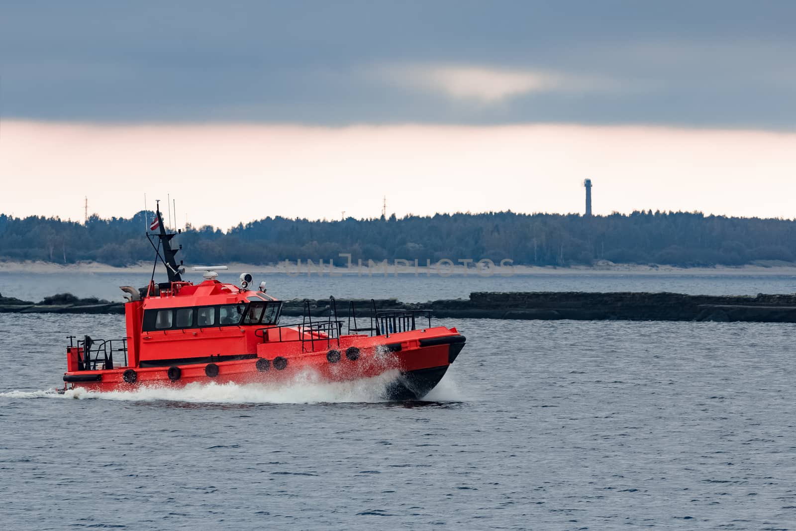 Red pilot ship moving at speed to Baltic sea in Riga, Europe