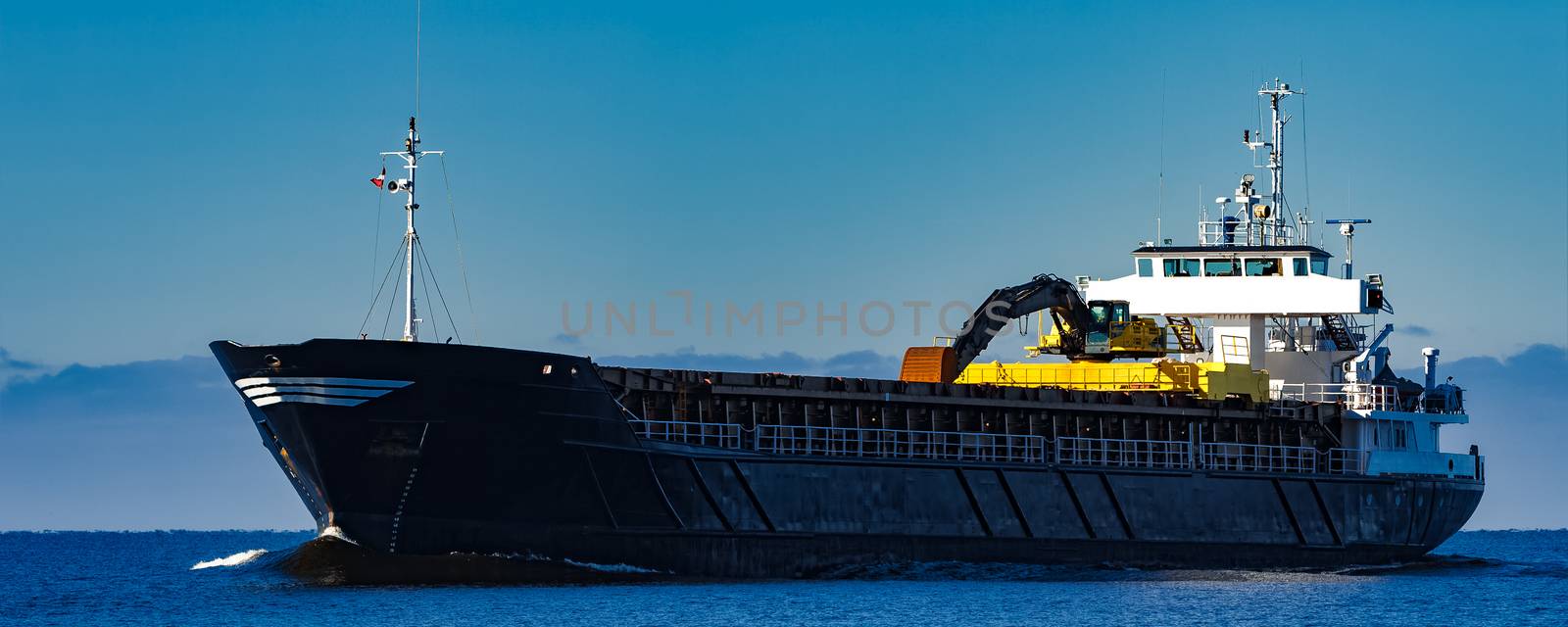Black cargo ship with long reach excavator moving by baltic sea