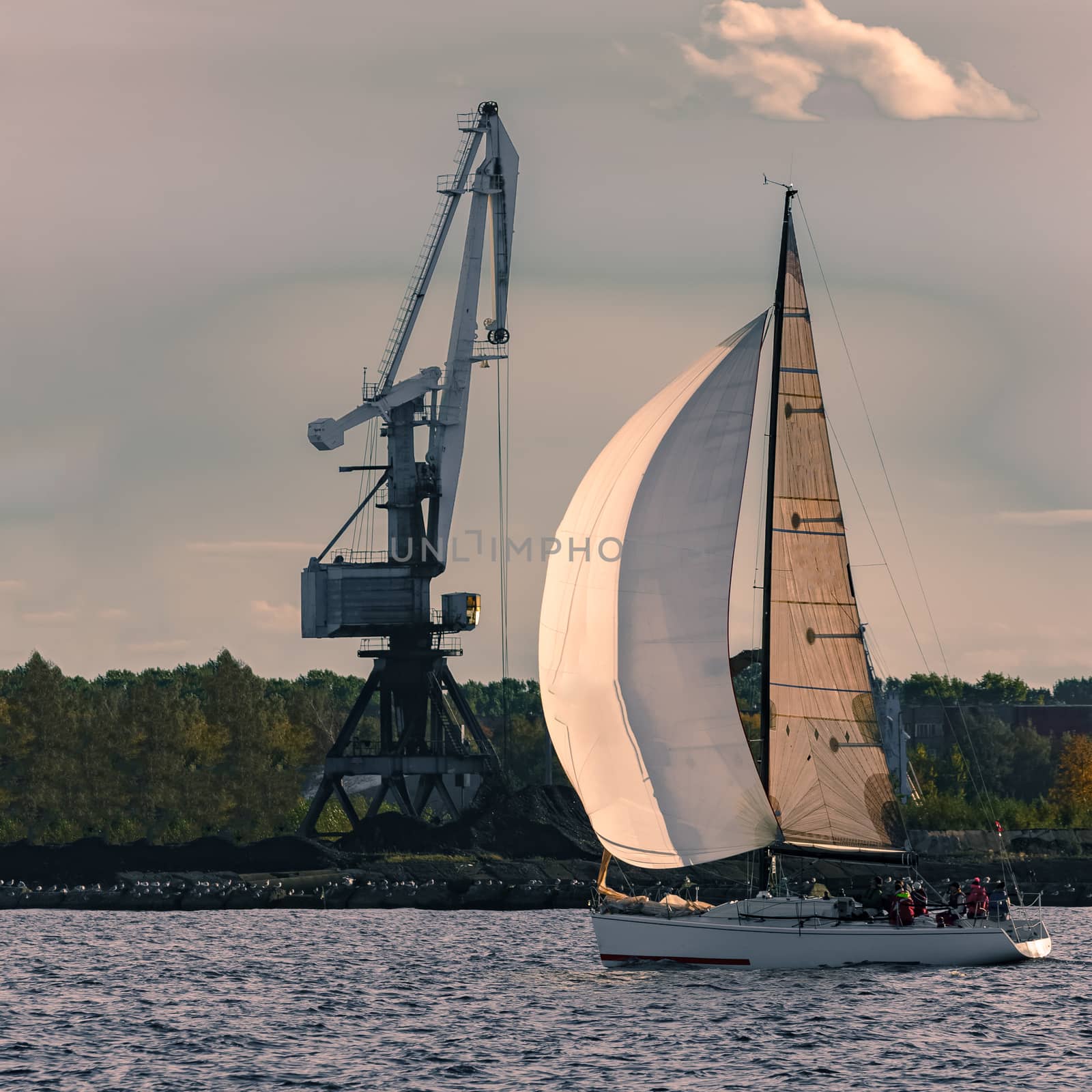 Sailboat moving past the cargo crane in evening, Latvia