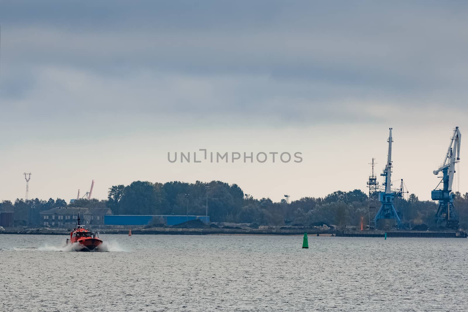 Red pilot ship moving at speed past the cargo cranes in Riga