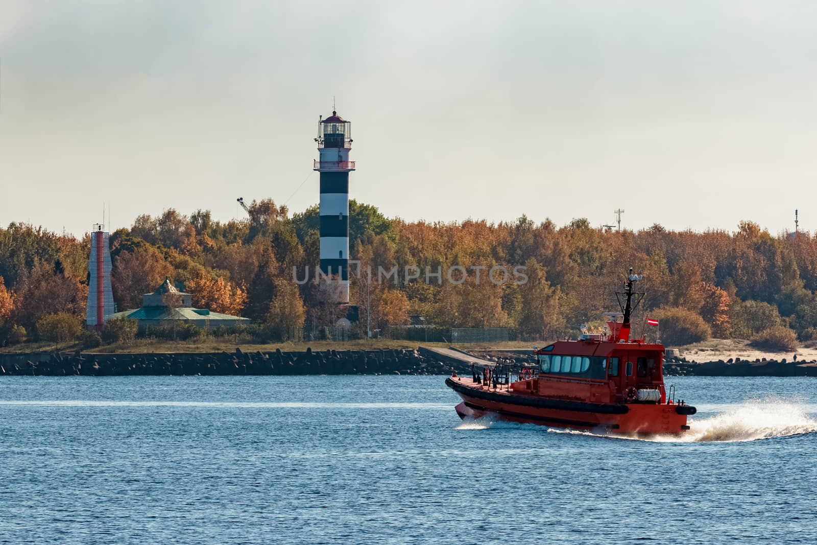 Red pilot ship moving at speed past the lighthouse in Riga
