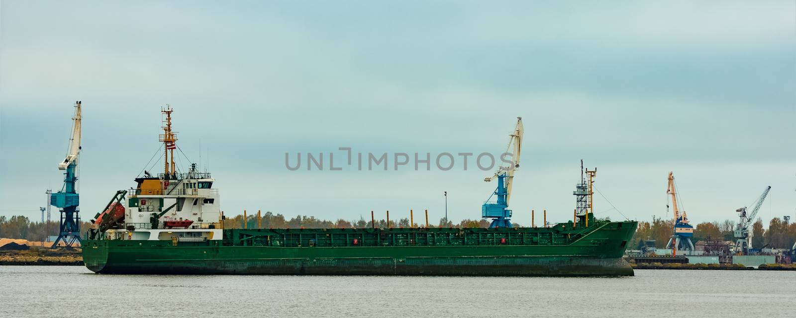 Green cargo ship moving to the port in cloudy day