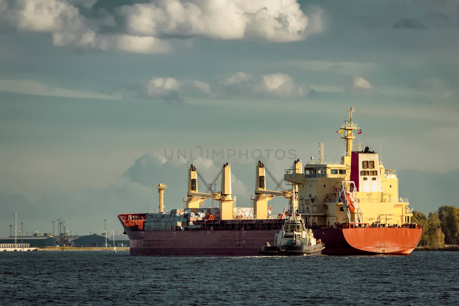 Red cargo ship and the tug ship towing it to the port