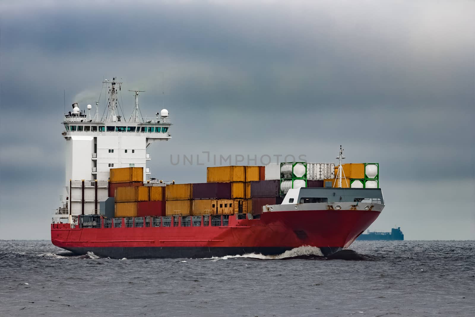 Red cargo container ship sailing from Baltic sea in cloudy day