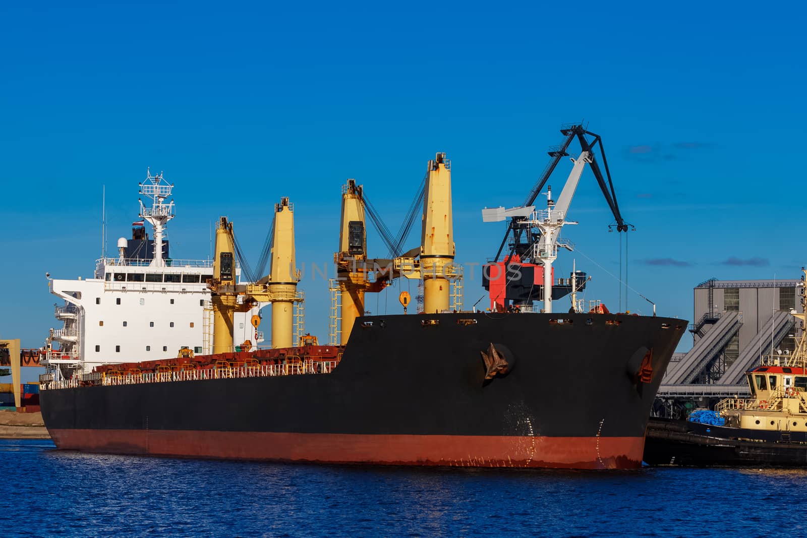 Black cargo ship mooring at the port with tug ship support