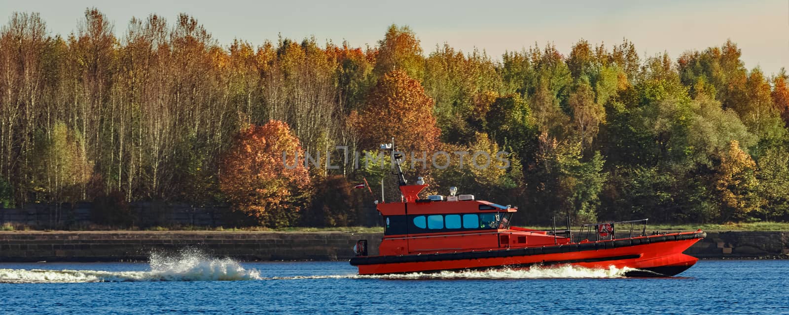 Red pilot ship moving past the autumn trees in Europe