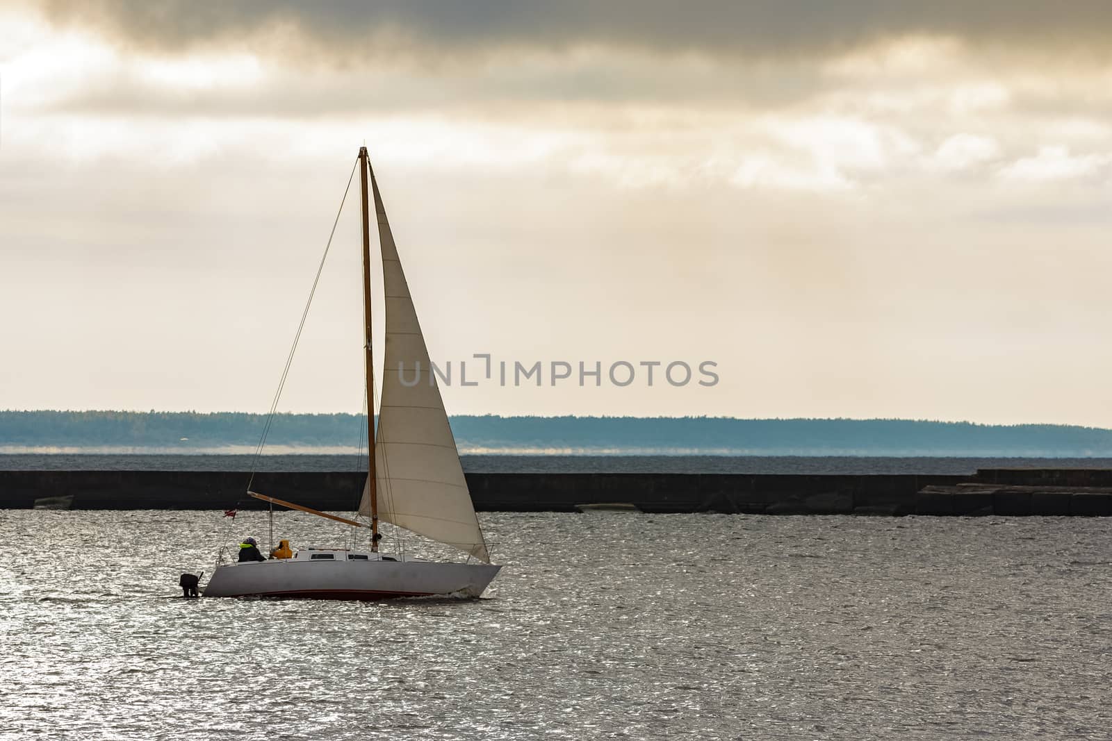 Small white sailboat traveling against breakwater dam